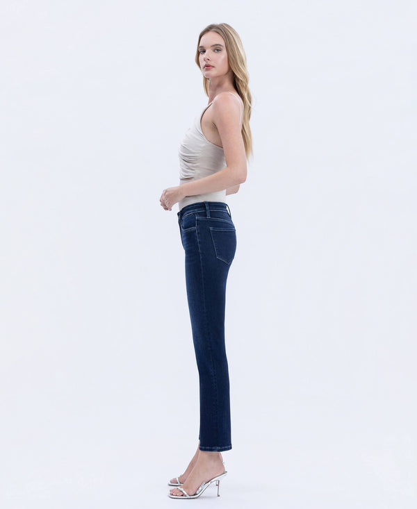 Woman wearing dark wash straight-leg jeans with a fitted silhouette, shown in side view paired with a neutral sleeveless top and heels.