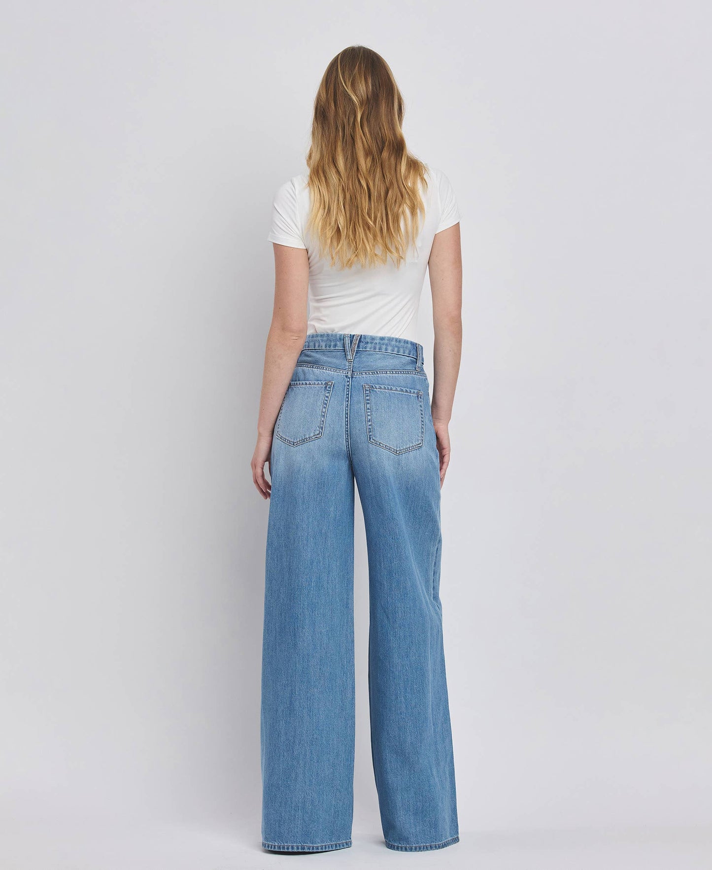 Person wearing blue jeans and a white shirt on a plain background
