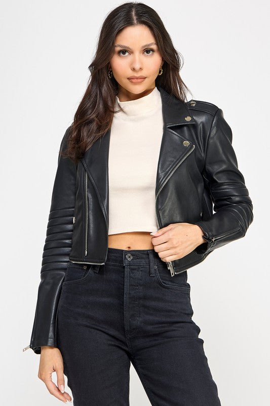 Woman wearing a black leather jacket over a white turtleneck and black jeans on a white background