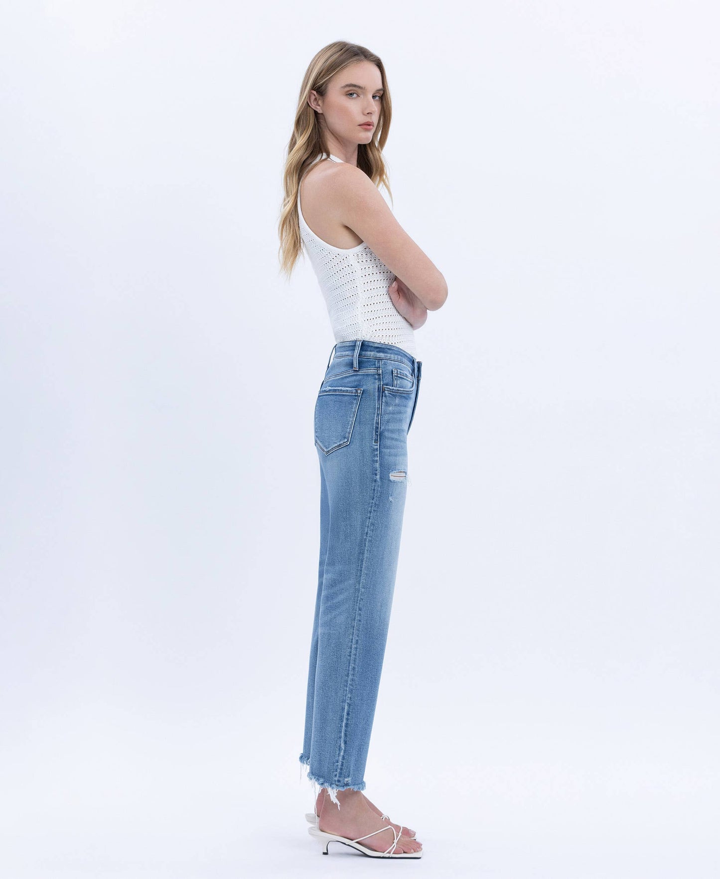 Woman wearing a white tank top and light blue jeans on a white background