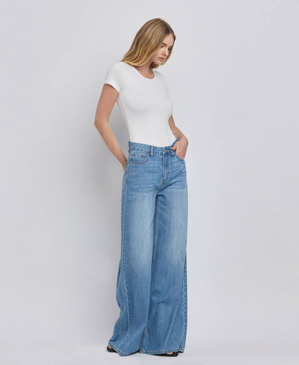 Woman wearing a white top and blue jeans on a plain background