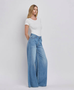 Woman wearing a white top and blue jeans on a plain background
