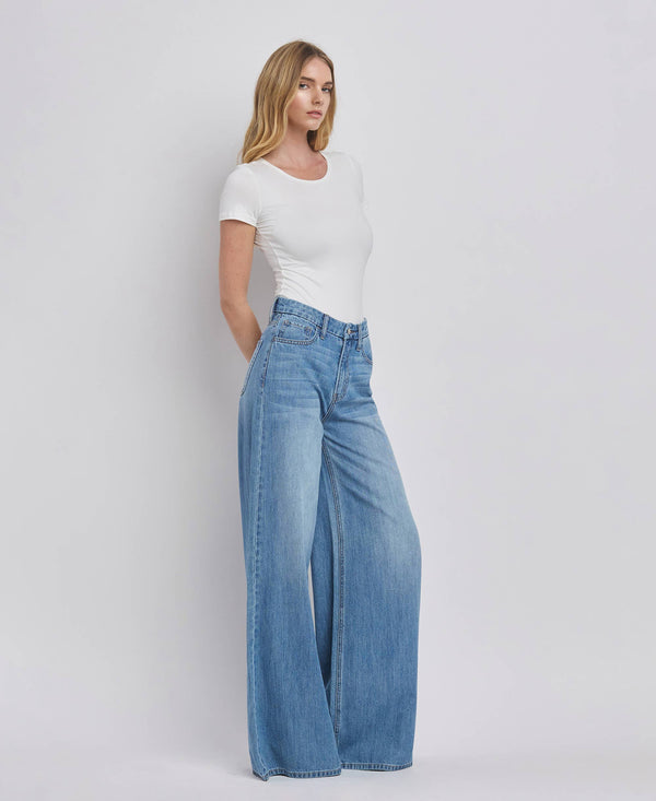 Woman wearing a white top and blue jeans on a plain background