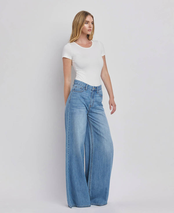 Woman wearing a white t-shirt and blue jeans against a plain background