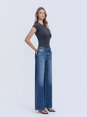 Woman wearing a dark gray t-shirt and blue jeans on a light gray background