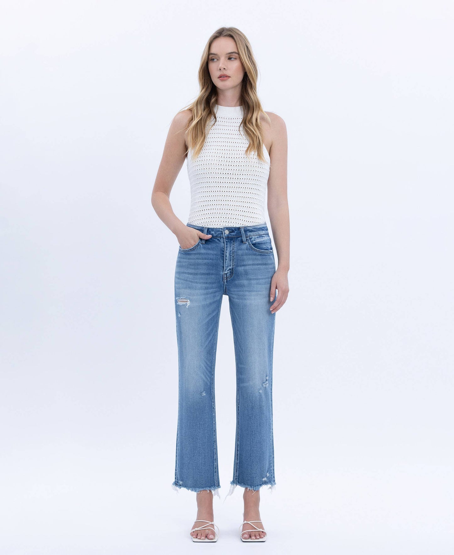 Woman wearing a white sleeveless top and blue jeans on a white background