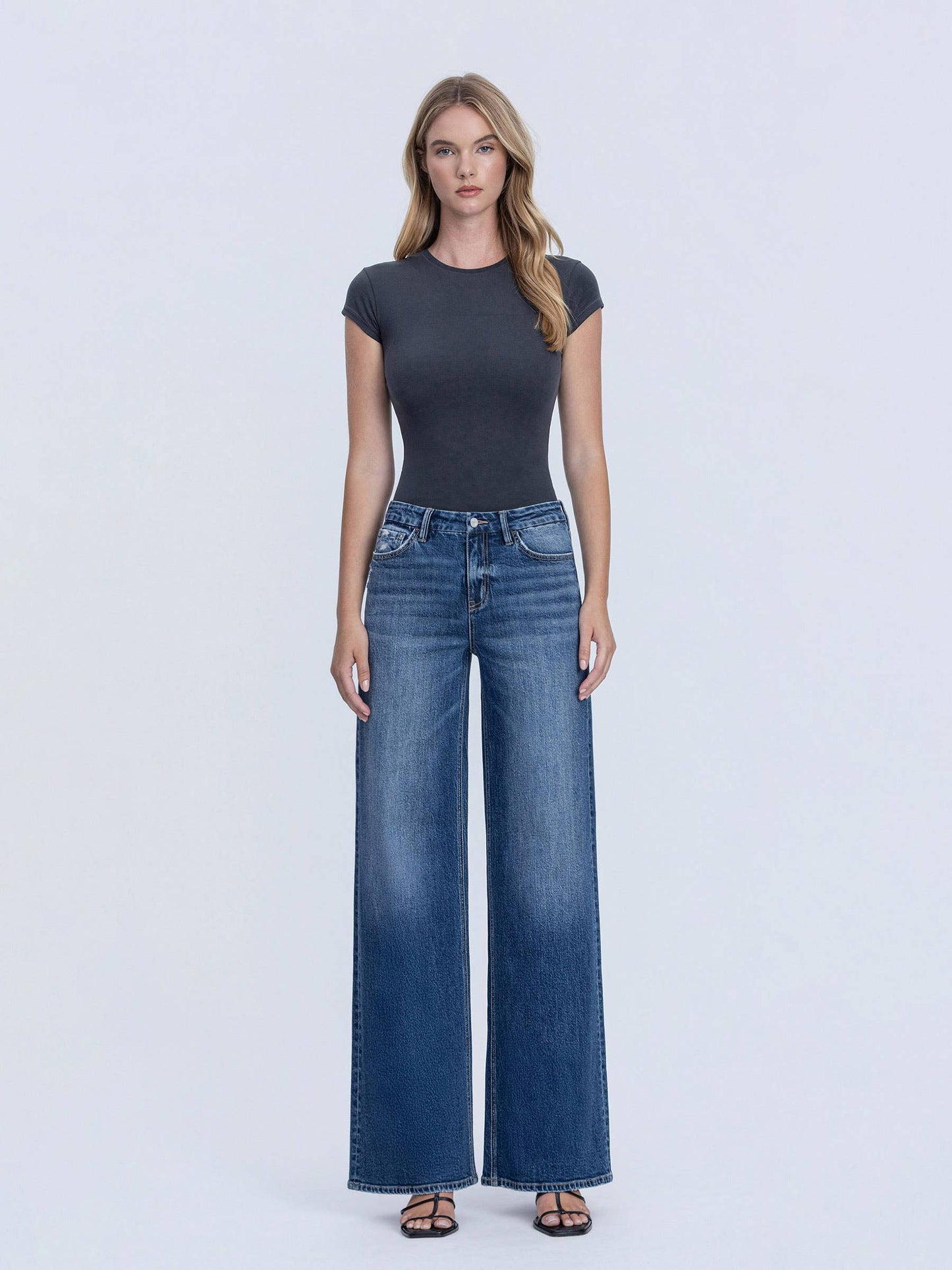 Woman wearing a dark gray t-shirt and blue jeans on a white background