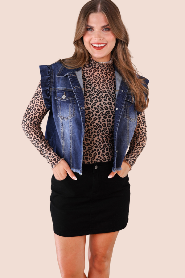 Woman wearing a leopard print top, black skirt, and denim vest on a beige background