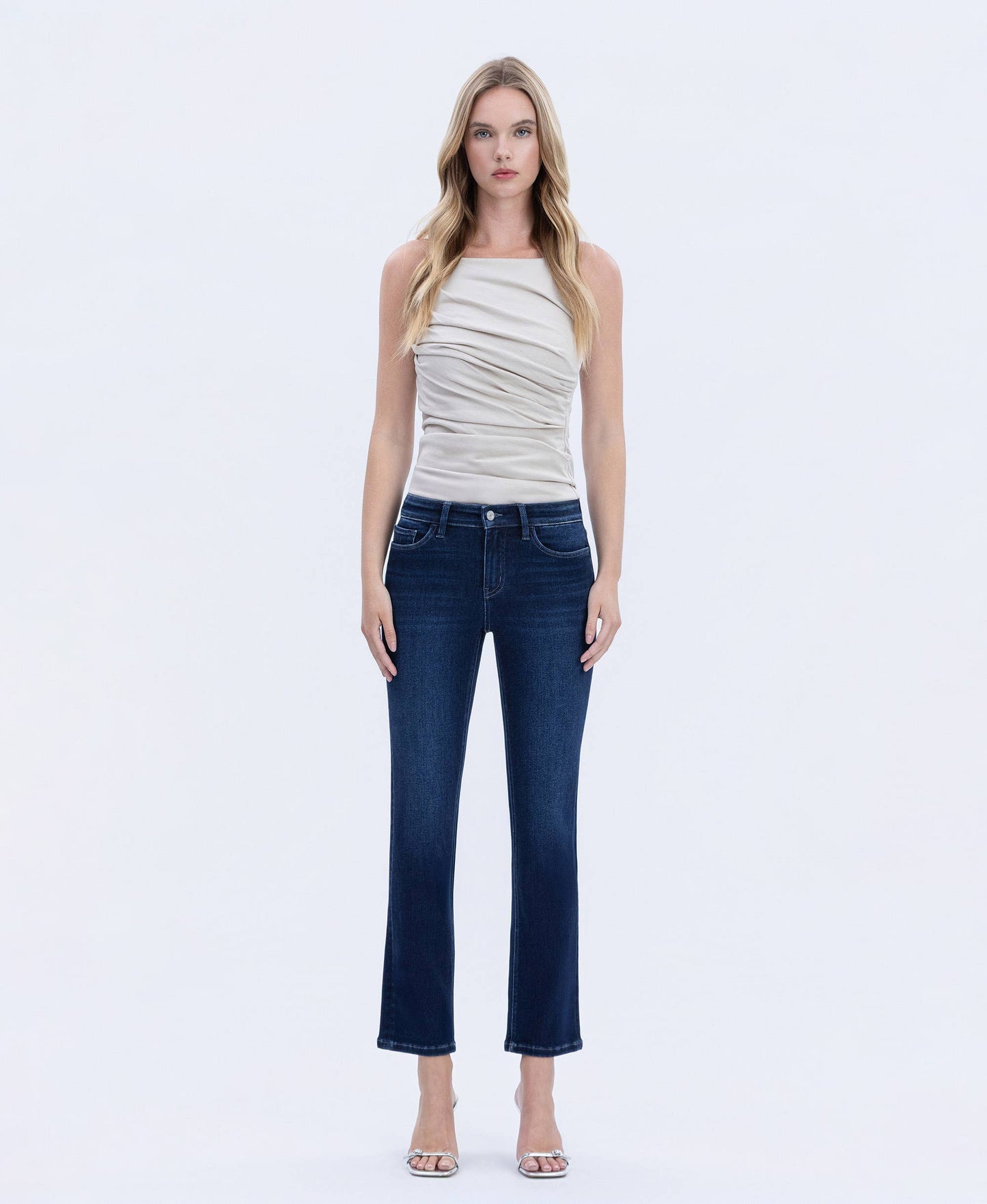 Woman wearing dark wash straight-leg jeans with a flattering mid-rise fit, styled with a neutral ruched sleeveless top, shown in front view.