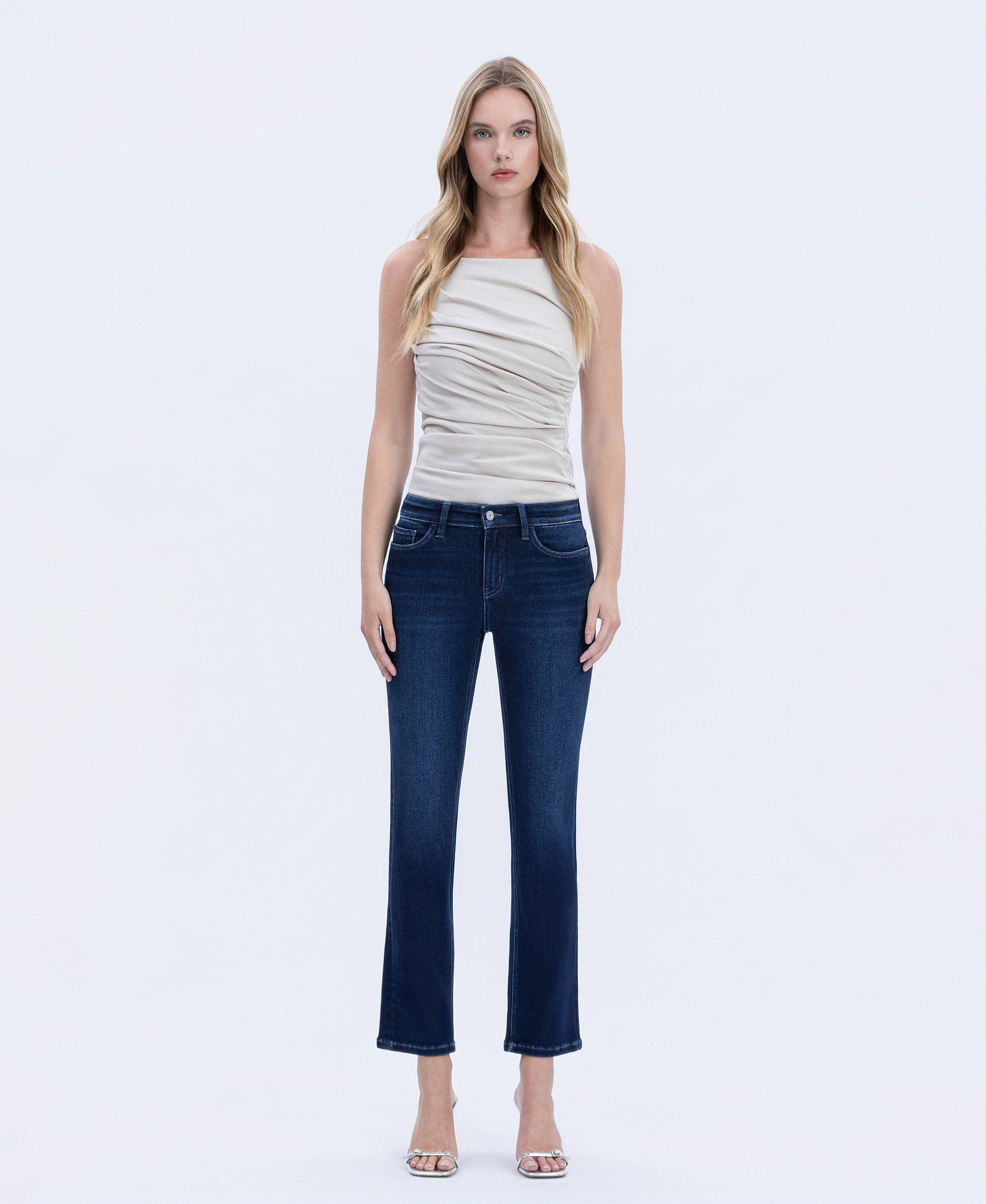 Woman wearing dark wash straight-leg jeans with a flattering mid-rise fit, styled with a neutral ruched sleeveless top, shown in front view.