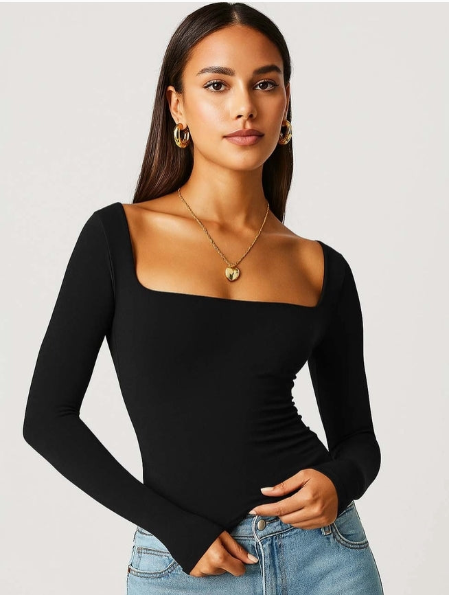 Woman wearing a black long-sleeve top and blue jeans against a plain background
