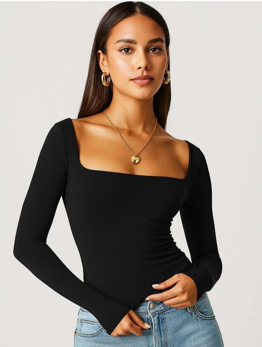 Woman wearing a black long-sleeve top and blue jeans against a plain background