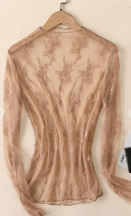 Sheer blouse with floral embroidery on a hanger against a white background