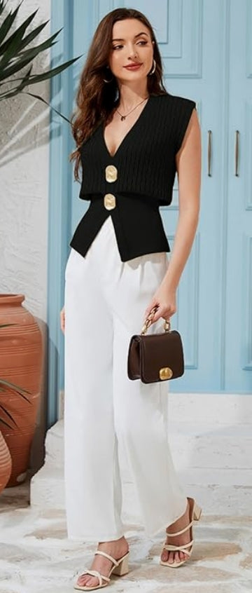 Woman in black sleeveless top and white pants holding a brown handbag against a light blue wall.