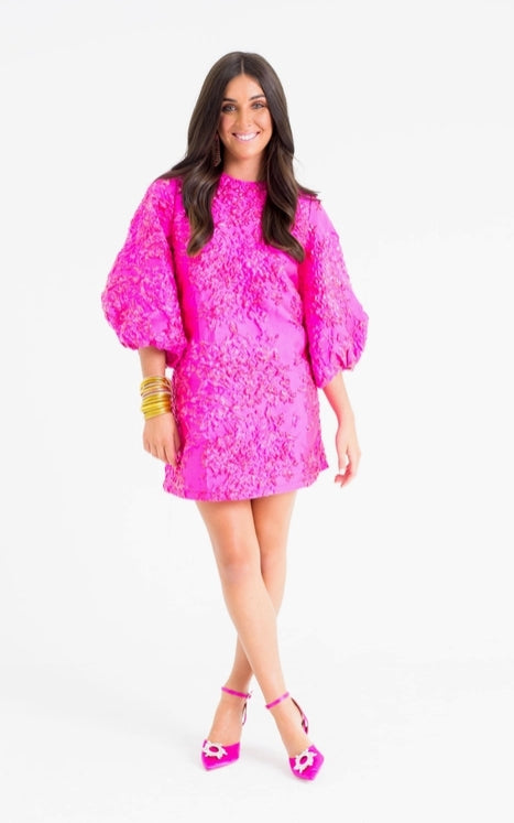 Woman wearing a bright pink dress with puffed sleeves on a white background