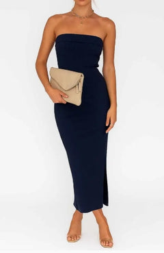 Woman wearing a strapless navy dress holding a beige clutch against a white background