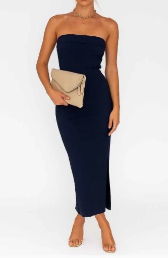 Woman wearing a strapless navy dress holding a beige clutch against a white background