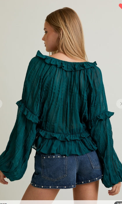 Woman wearing a teal blouse with ruffled details and denim shorts on a plain background