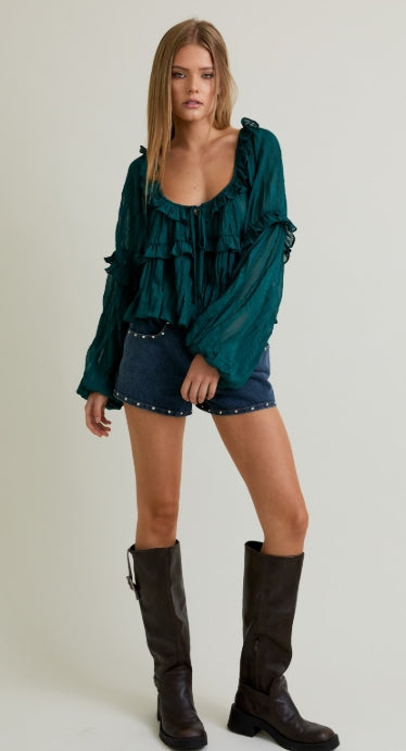 Woman wearing a green blouse, denim shorts, and brown knee-high boots on a white background