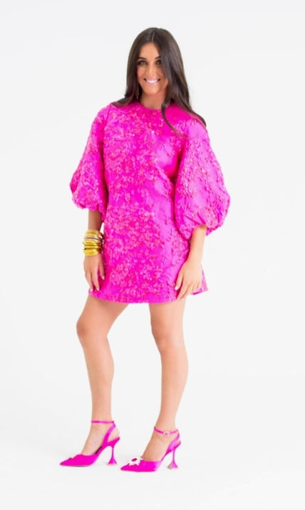 Woman wearing a bright pink dress with puffed sleeves on a white background