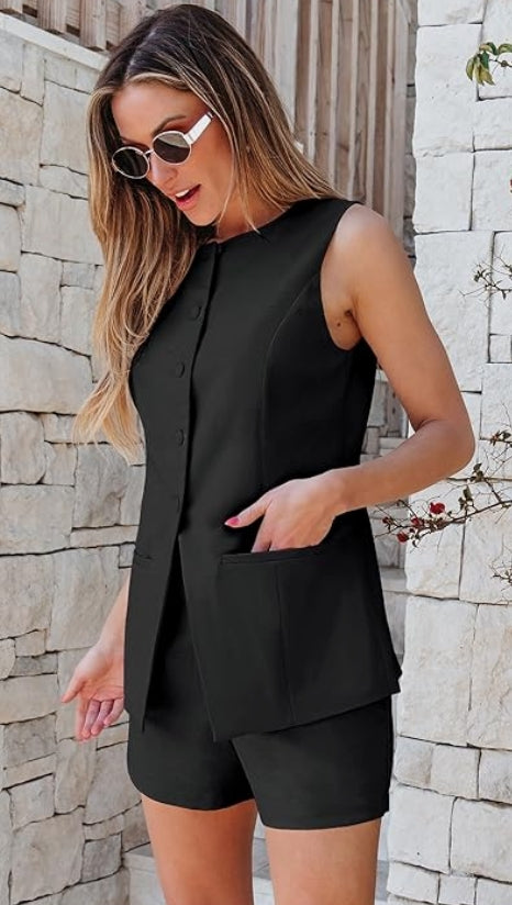 Woman wearing a black sleeveless top and shorts against a stone wall.