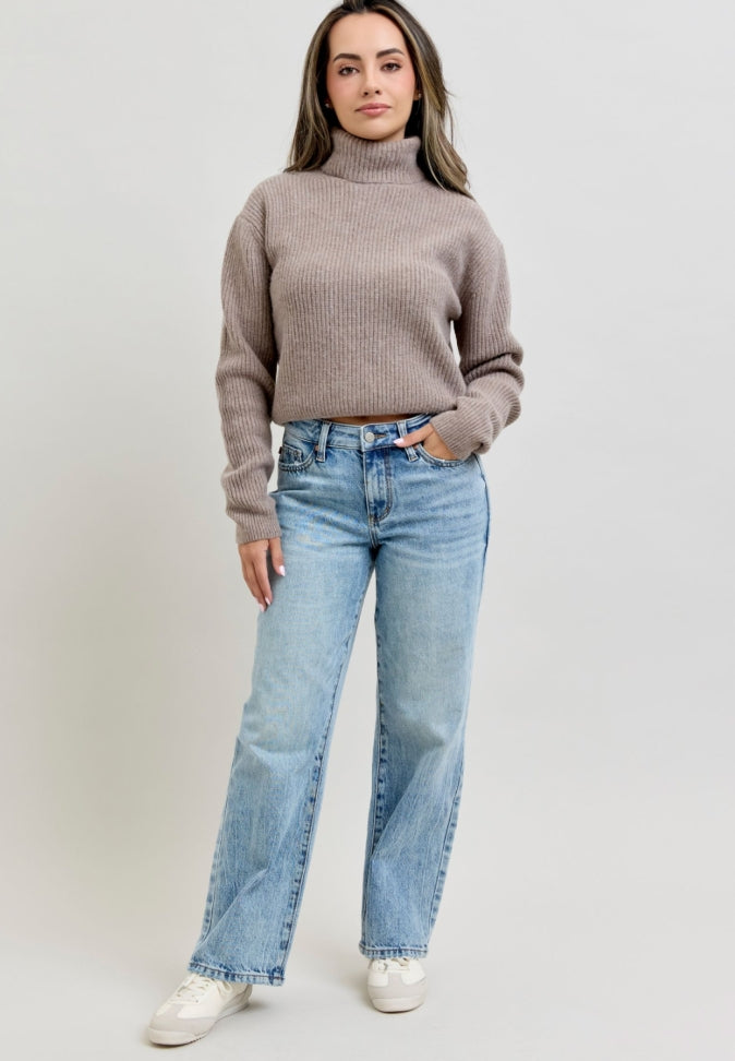 Woman wearing a brown sweater and light blue jeans on a plain background