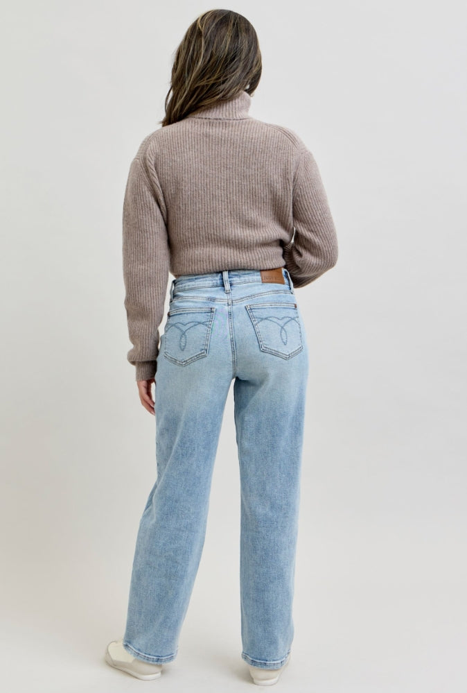 Person wearing a brown sweater and light blue jeans on a plain background