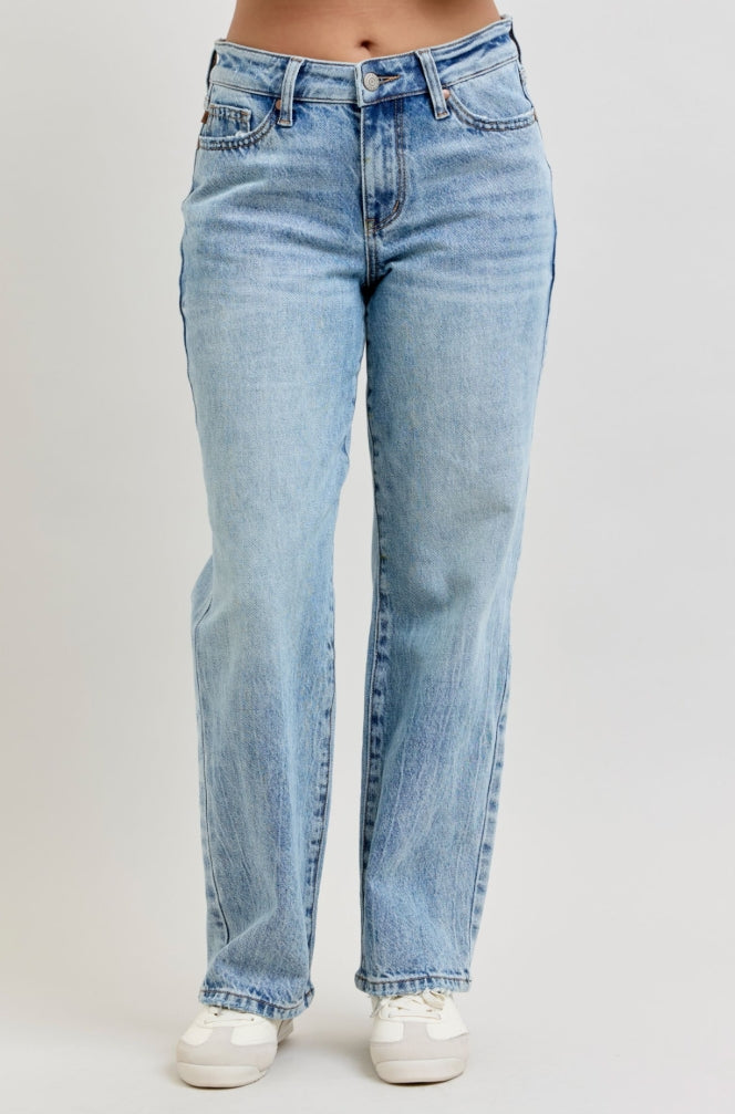 Woman wearing a brown sweater and light blue jeans on a plain background