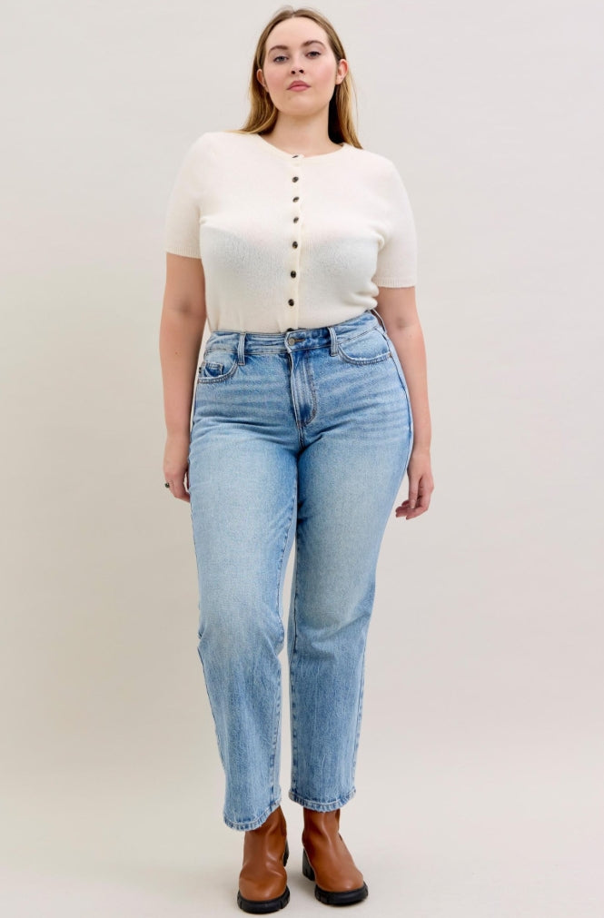 Woman wearing a white button-up shirt and light blue jeans on a plain background