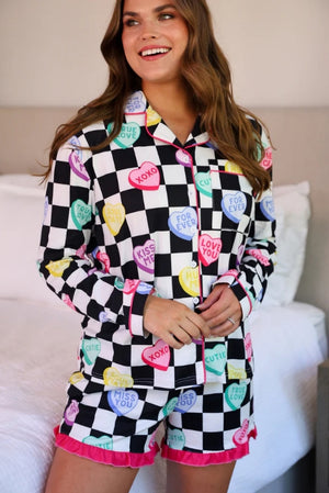 Woman wearing a checkered pajama set with colorful text patterns in a bedroom setting.
