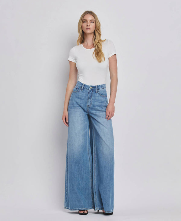 Woman wearing a white t-shirt and blue wide-leg jeans on a plain background