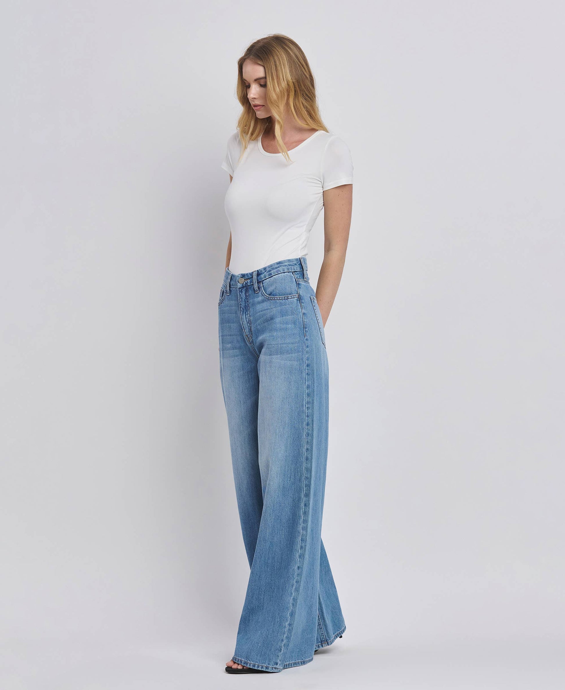 Woman wearing a white t-shirt and blue flared jeans on a plain background
