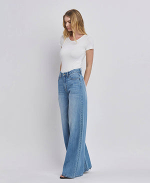 Woman wearing a white t-shirt and blue flared jeans on a plain background