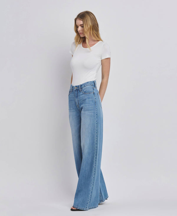 Woman wearing a white t-shirt and blue flared jeans on a plain background