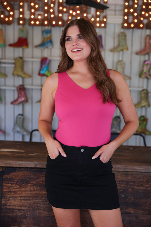 Woman wearing a pink tank top and black skirt standing in front of a wall with colorful boots.