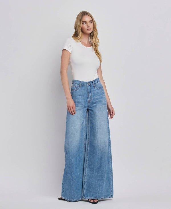 Woman wearing a white top and blue wide-leg jeans against a plain background