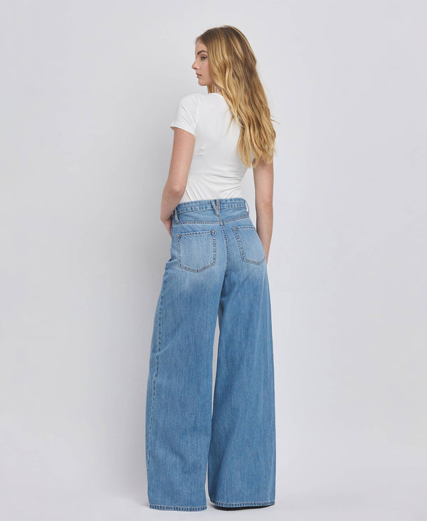 Woman wearing blue wide-leg jeans and a white t-shirt on a plain background