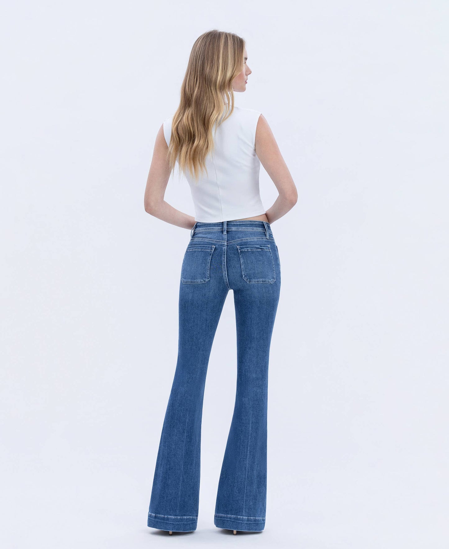 Woman wearing blue jeans and a white top on a light gray background
