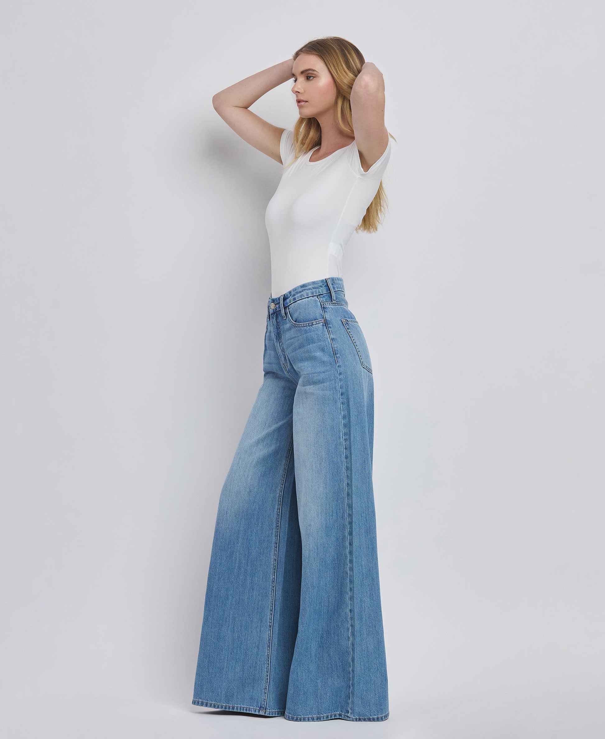Woman wearing a white top and blue jeans on a plain background