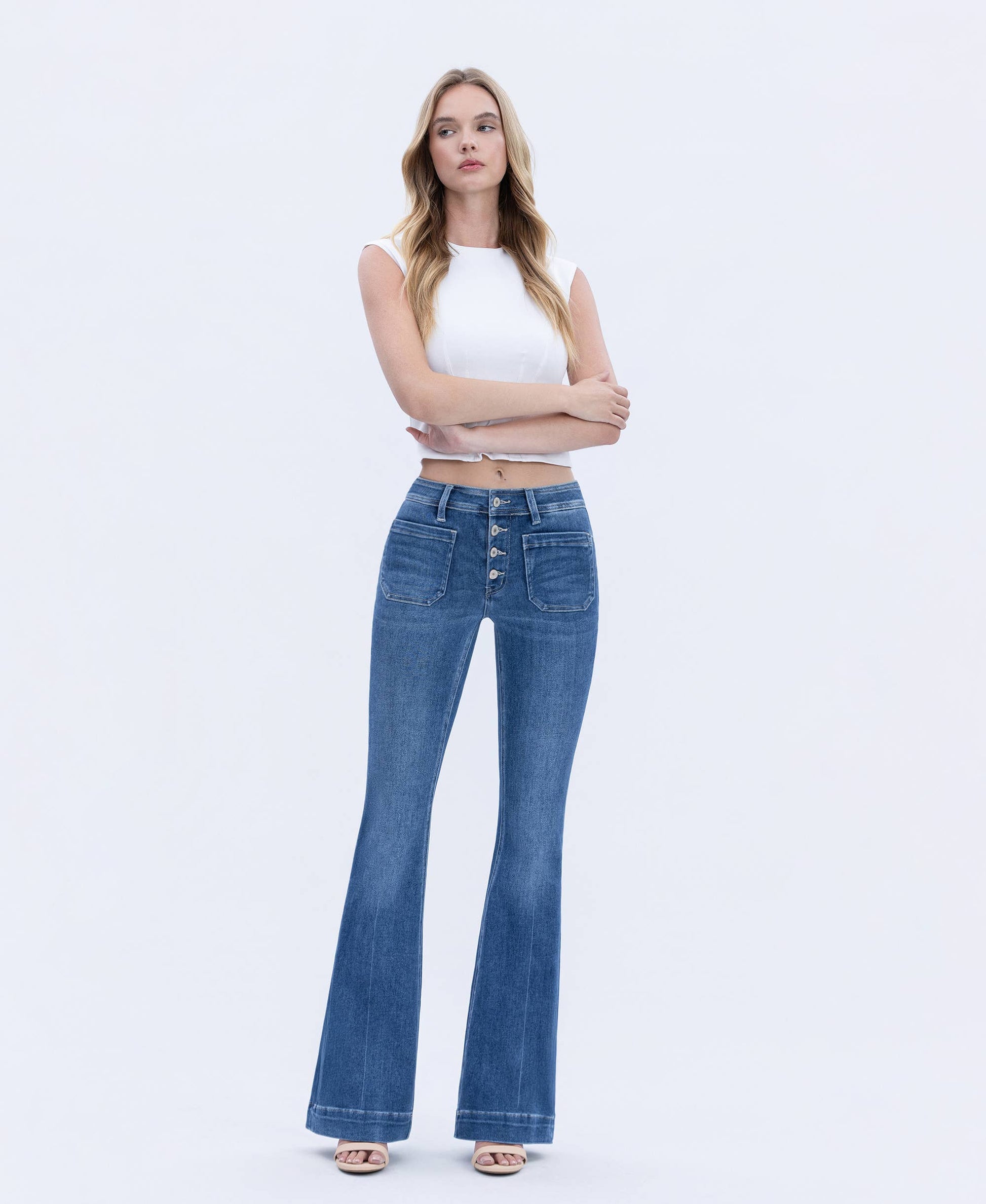 Woman wearing blue flared jeans and a white top on a light gray background