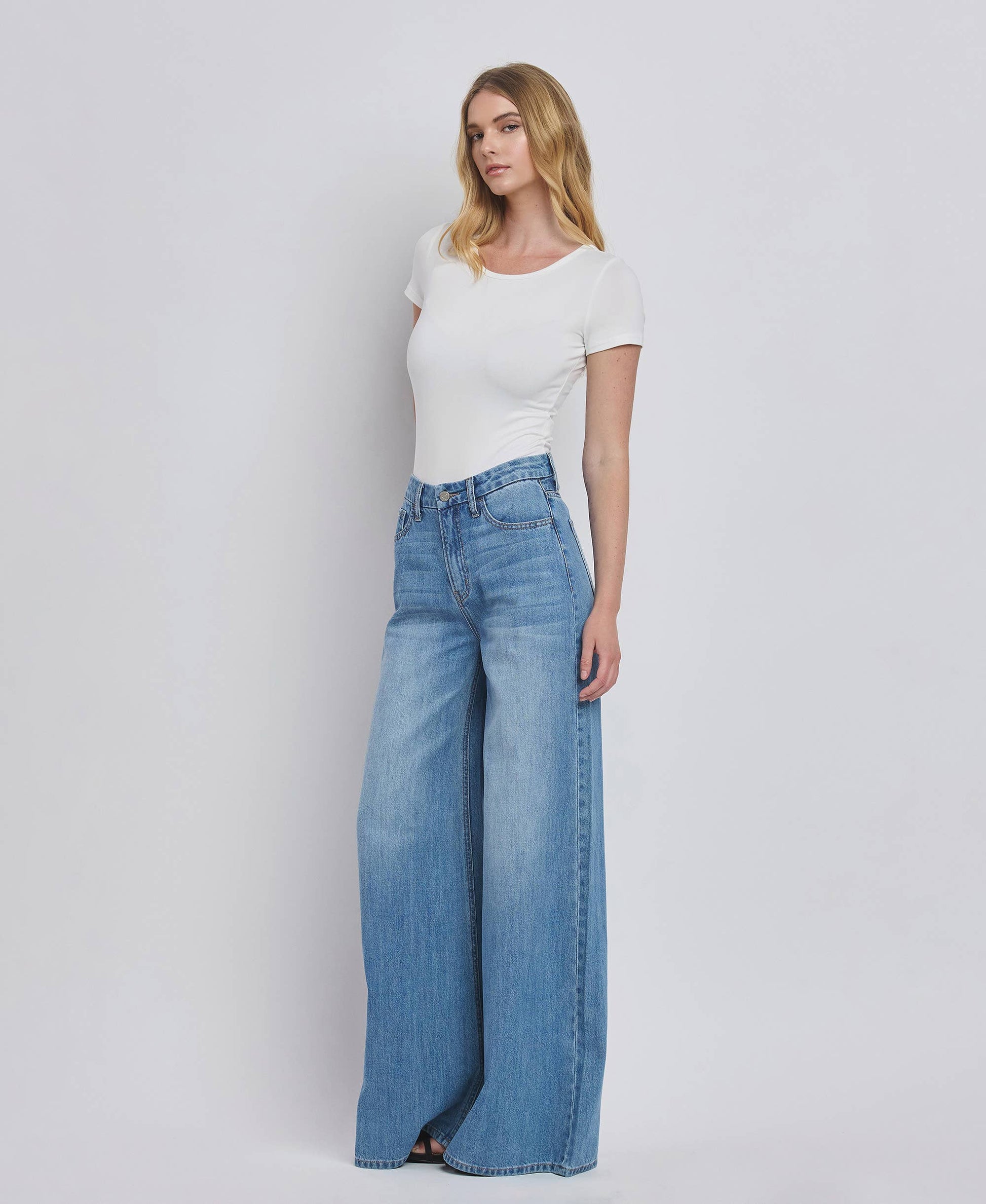 Woman wearing a white top and blue jeans on a plain background