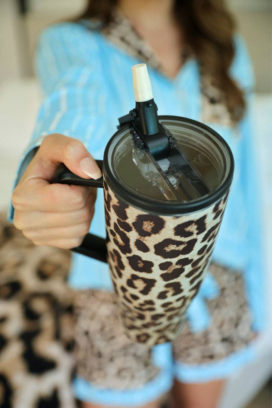 Person holding a leopard print mug with a straw attachment.